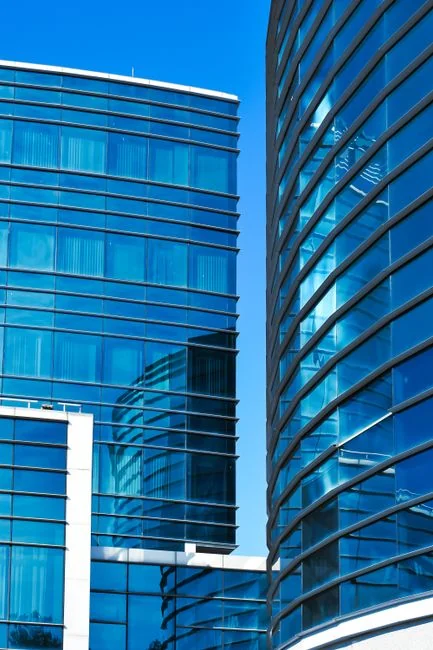 Three window cleaners suspended on ropes clean a modern glass building facade during the day.